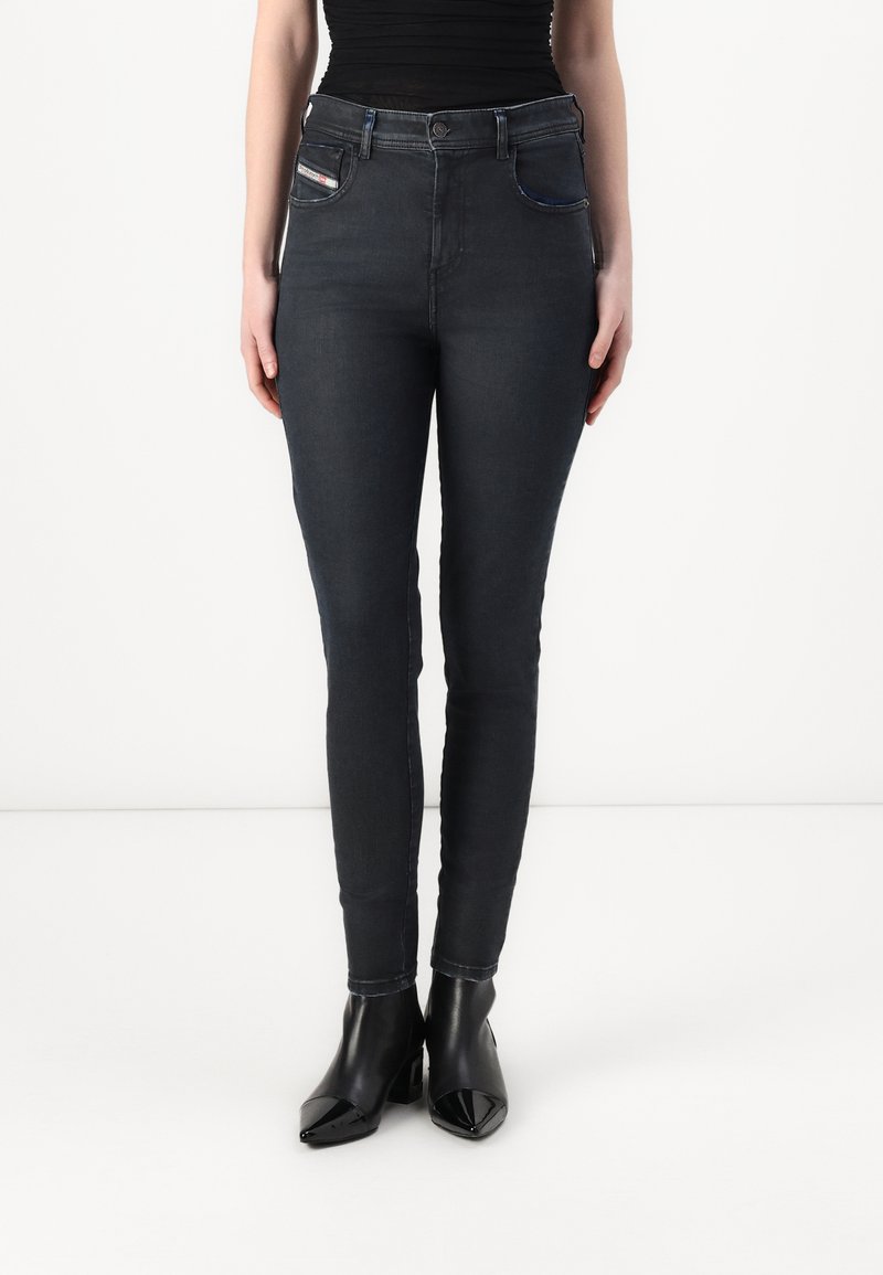 Jean skinny en denim foncé avec taille haute, dotés de poches avant et de coutures contrastées, associés à des bottines à talons noires.