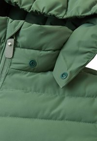 Zielona, ocieplana kurtka z zapięciem na zamek błyskawiczny, zatrzaskami oraz wysokim kołnierzem. Posiada gładką, błyszczącą teksturę i pionowy wzór przeszyć.