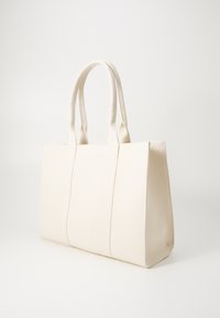 Vit canvas toteväska med två robusta handtag, rektangulär design och synliga sömmar. Har en strukturerad form och en slät textur.