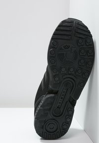 Black athletic sneaker with a textured rubber sole featuring circular patterns and grooves, designed for traction and support.