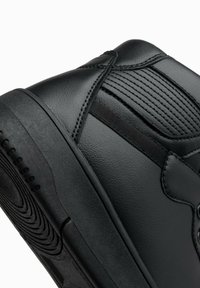 Sneakers montants noirs avec une extérieure en synthétique lisse, un panneau texturé et une semelle en caoutchouc durable avec un design de semelle circulaire.