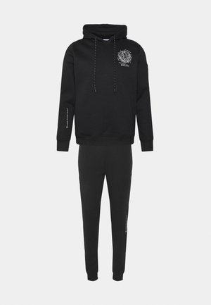 Conjunto de sudadera con capucha negra y pantalones deportivos a juego con estampado geométrico blanco en el pecho y detalles de texto en la manga y la pierna del pantalón.