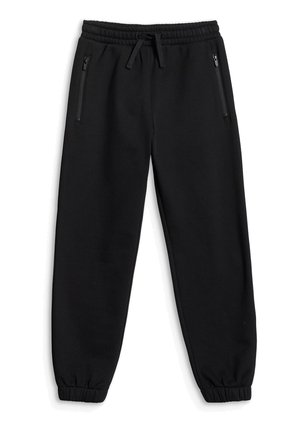 Chłopiec w czarnej koszulce Champion z małpką w kimonie karate, czarne spodnie, białe tenisówki, trzyma neonowo zieloną bluzę z kapturem na szarym tle.