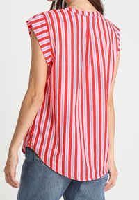 Punavalkoraidallinen lyhythihainen paita, jossa on pyöreä helma ja takaosassa laskos lisäämässä mukavuutta ja rentoa istuvuutta.