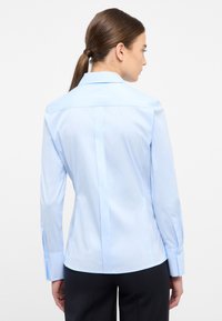 Light blue shirt with a smooth, shiny texture, featuring a pointed collar and long sleeves with buttoned cuffs. Tailored fit with back seam details.
