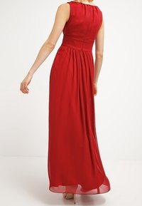 Abito maxi rosso con busto aderente, design senza maniche e gonna fluida. Tessuto morbido con un leggero luccichio, dettaglio in vita arricciato.