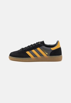 Czarno-żółty sneaker Adidas Spezial z gumową podeszwą, trzema żółtymi paskami i wiązaniem na sznurówki, pokazany z boku na białym tle.