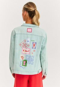 Jasnoniebieska kurtka dżinsowa z kolorowymi naszywkami, w tym wzorami kwiatowymi i napisem. Zaprojektowana z kołnierzem i guzikami na mankietach.