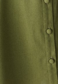 Tessuto verde oliva con una consistenza liscia, presenta una fila di bottoni arrotondati lungo un lato. Design semplice e minimalista.