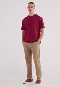 T-shirt rossa a maniche corte con scollatura rotonda, abbinata a chinos beige e scarpe marroni, caratterizzata da un design semplice e classico.