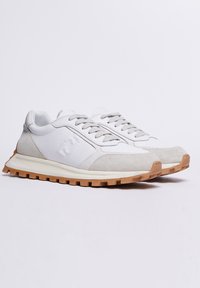Sneaker bianchi e grigi con parte superiore texture, suola in gomma e chiusura con i lacci. Presentano un accento con logo sul lato e una soletta ammortizzata.