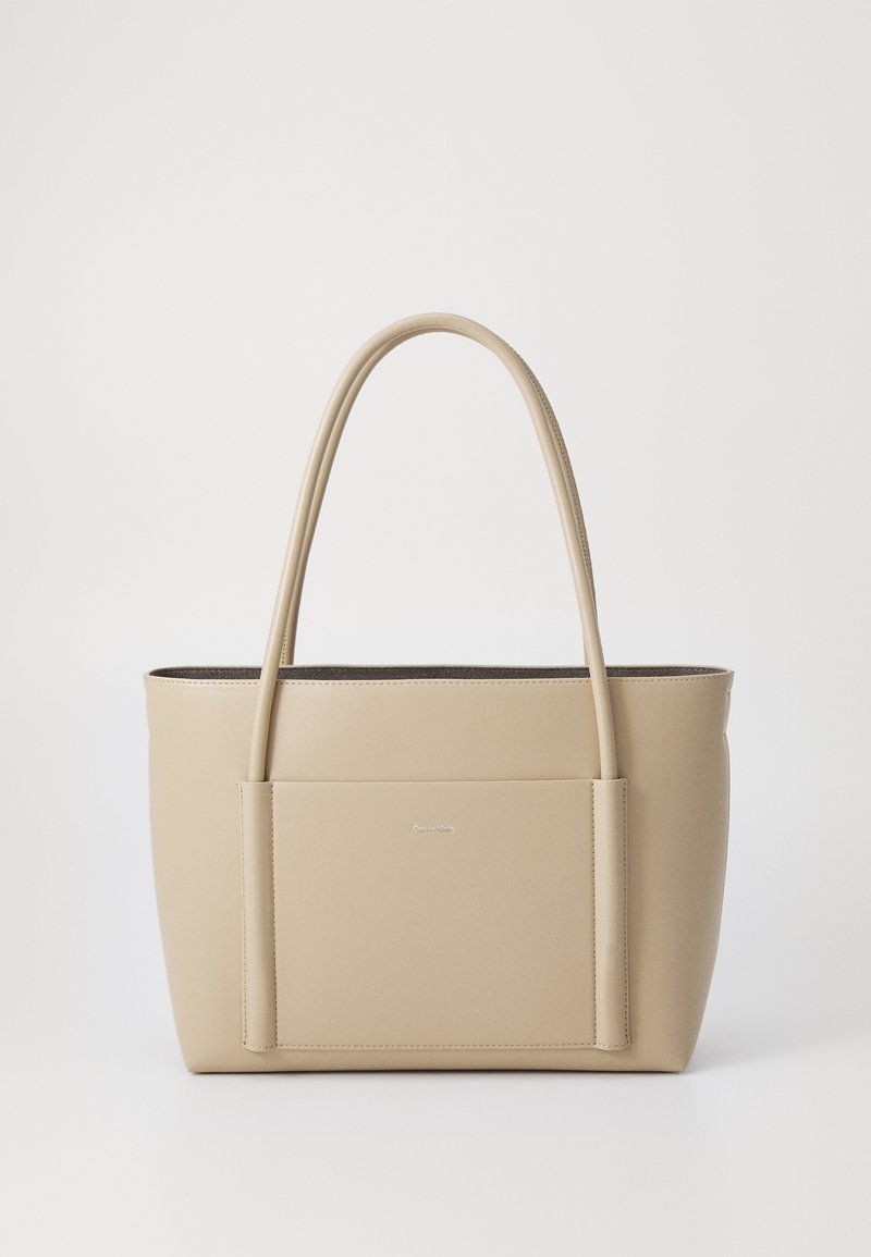 Borsa a tracolla beige realizzata in materiale liscio, dotata di due manici lunghi, una tasca frontale e un design minimalista con un piccolo logo del marchio.