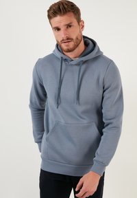 Pull-over en capuche bleu clair, fabriqué en mélange de coton doux. Il dispose d'une poche kangourou à l'avant, d'une capuche avec cordon de serrage ajustable et de poignets côtelés.