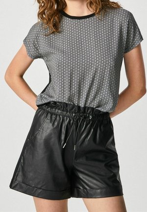 Frau trägt ein schwarz-weiß gemustertes Kurzarm-T-Shirt, das in hoch taillierte schwarze Leder-Shorts mit Tunnelzugbund gesteckt ist.