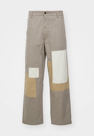 Béžové široké nohavice s patchwork dizajnom s jasnými a tmavými častami látky; obsahujú štvorcové akcenty a predné zapínanie na gombík.