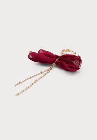 Gold hoop earring with dark red fabric bow and two gold chains of different lengths hanging from the center of the bow.