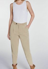 Top sans manches blanc avec un éclat texturé associé à un pantalon beige taille haute légèrement fuselé, comportant une poche avant et une fermeture à bouton.