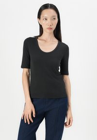 Zwarte korte mouwtop met een ronde halslijn, geribbelde textuur en een aansluitend ontwerp. Draag met blauwe high-waisted broek, minimalistische stijl.