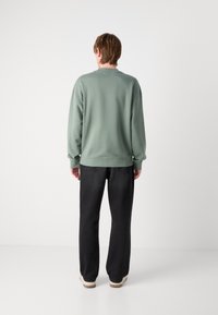 Sudadera verde con mangas largas, puños y dobladillo acanalados; combinada con pantalones negros de pierna recta y zapatos beige. Diseño simple y relajado.