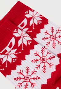 Κόκκινες και λευκές κάλτσες με ριχτή υφή, που φιλοξενούν σχέδια χιονονιφάδας και γεωμετρικά σχέδια σε όλη την επιφάνεια.