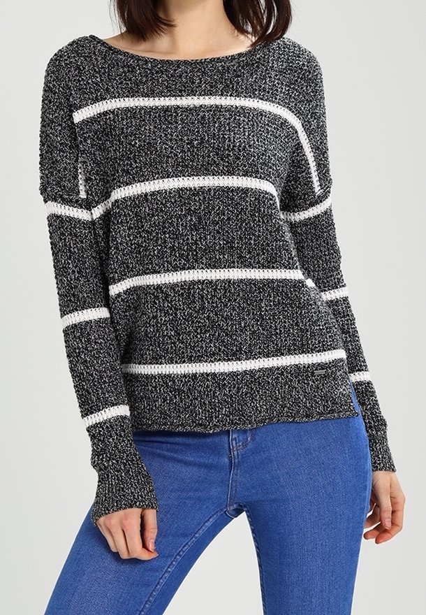 Schwarz-weißer gestreifter Strickpullover mit langen Ärmeln, weitem Ausschnitt und gerippten Bündchen. Getragen über blauen Jeans.
