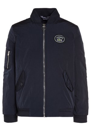 Marineblauw bomberjack met ritssluiting aan de voorkant, twee klepzakken, een ritssluitingzak op de mouw en een Lacoste-logo op de borst.