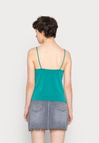 Camisola ajustada em verde-água com alças finas, feita de um tecido suave, combinada com uma saia de ganga cinza com bainha desfiada e bolsos traseiros.