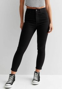 High-waisted black skinny jeans in denim with a smooth texture, paired with black high-top sneakers featuring white soles and laces.