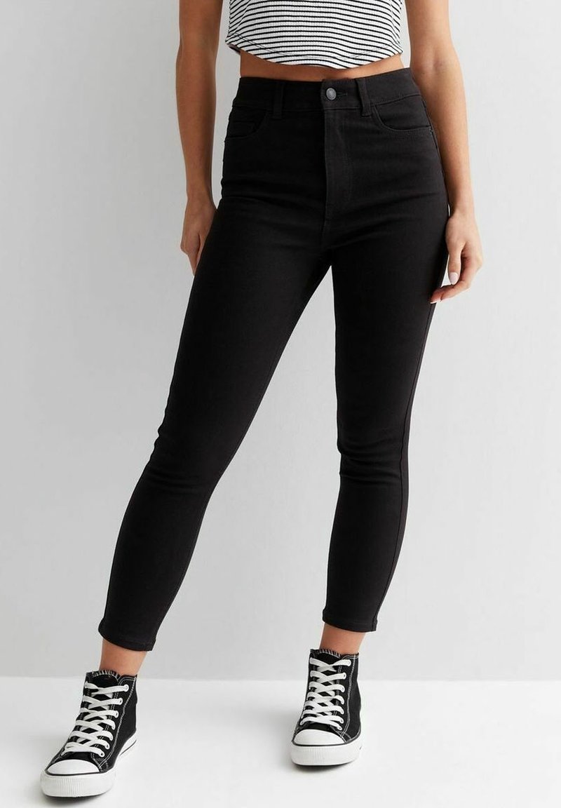 High-waisted black skinny jeans in denim with a smooth texture, paired with black high-top sneakers featuring white soles and laces.