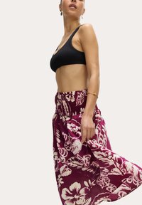 Top corto nero a coste e gonna maxi floreale bordeaux con vita smock, caratterizzata da motivi bianchi di ibisco su un tessuto fluido.