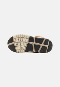 Schoenzool van zwart rubber met beige accenten, met een gestructureerd patroon voor grip en verhoogde secties voor flexibiliteit en ondersteuning.
