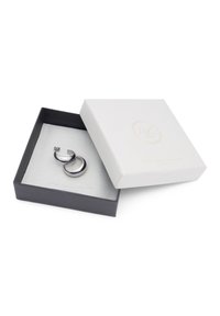 Colgante de plata de ley con un acabado brillante, que presenta un diseño curvado. Presentado en una caja de joyería en blanco y negro con una superficie texturizada.