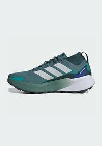 Scarpe da trail running con tomaia in rete teal e verde scuro, tre strisce bianche e suola in gomma testurizzata per una maggiore aderenza.
