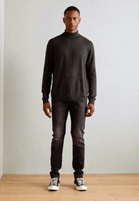 Mørkegrå turtleneck sweater parret med mørke jeans og sorte og hvide sneakers. Det samlede look er monochromatisk med en slim fit.