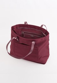 Bordeaux kleurige tote bag met een met rits afgesloten binnenzak, dubbele handvatten en een externe voorzak. Gemaakt van duurzaam fabric met een soepele textuur.