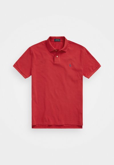 Polo vermelho feito de algodão, com colarinho canelado, abertura de dois botões e um pequeno logotipo bordado no lado esquerdo do peito.