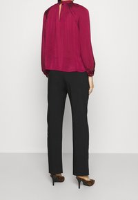 Blusa bordeaux a maniche lunghe con dettaglio a chiave nella parte posteriore e spalle arricciate, abbinata a pantaloni neri e tacchi con stampa animalier.