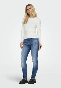 Chemise blanche à manches longues associée à un jean skinny bleu déchiré. Les chaussures comportent des semelles épaisses noires. Design simple et décontracté avec des détails subtils.