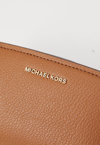 Ruda tekstūruota odos danga su auksiniu "MICHAEL KORS" logotipu. Dizainas elegantiškas, su subtiliu, smulkia grūdo raštu.