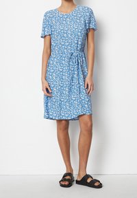 Kortärmad blå klänning med vit blommönster, åtsittande i midjan, knälång, tillsammans med svarta platta sandaler.