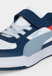 Бяла, тъмносиня, светлосива и червена маратонка Puma с връзки и тъмносиня велкро лента на бял фон.