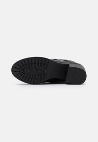 Suela de zapato negra con una superficie texturizada y con patrones, que presenta agarres de tracción y un diseño de taco. Acabado liso sin marcas visibles.