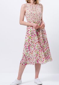 Robe midi fleurie en tissu léger et transparent, ornée d'un mélange de fleurs roses, vertes et jaunes. Design sans manches avec une ceinture à la taille.