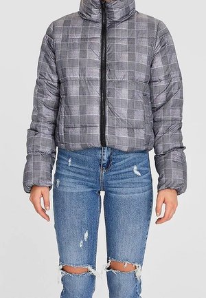 Grijze geruite pufferjas met rits aan de voorkant, gedragen met versleten blauwe gescheurde jeans met knieën zichtbaar.