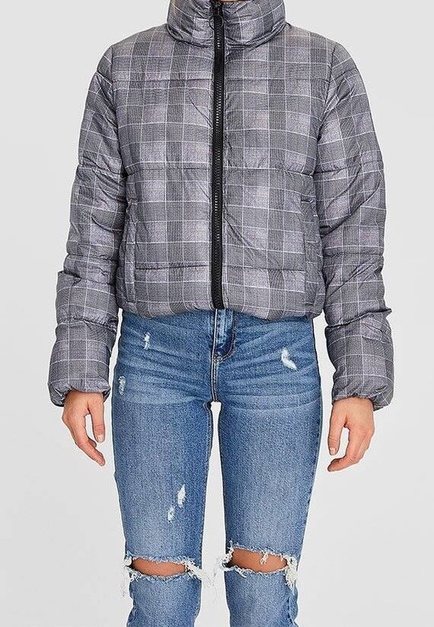 Doudoune grise à carreaux avec zip à l'avant portée avec un jean bleu déchiré usé montrant les genoux.
