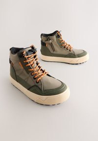 Bottes de randonnée vert olive avec des accents orange, dotées d'un design robuste, d'une tige textile, d'une semelle en caoutchouc et d'une fermeture éclair latérale pour l'accessibilité.