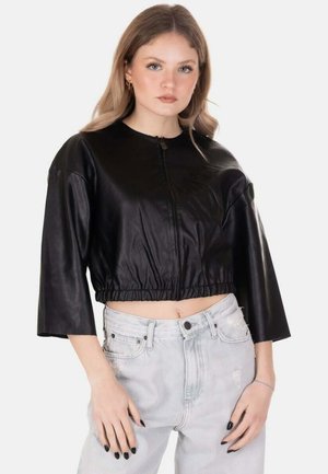 Giovane donna con capelli chiari indossa una giacca di pelle nera corta con maniche a mezze braccia e jeans chiari a vita alta.