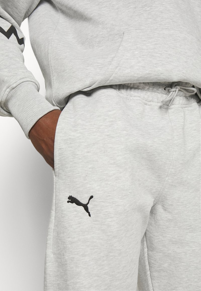 Pantaloni sportivi grigi chiari realizzati in materiale morbido, con elastico in vita, tasche laterali e logo Puma nero sulla coscia sinistra.