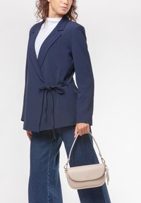 Blazer navy con cintura legata, vestibilità su misura e colletto a revers. Abbinato a denim a gamba larga e una borsa beige chiaro con una forma strutturata.