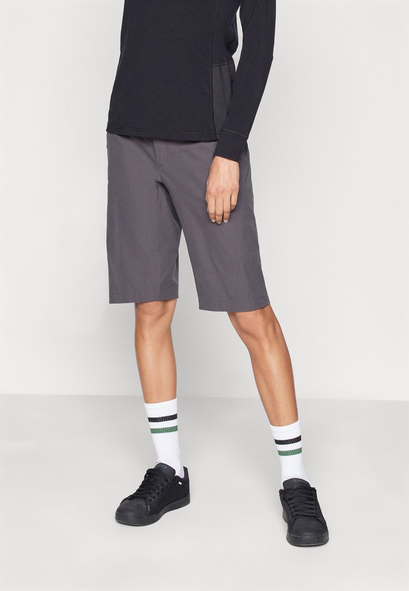 Grå knelange shorts laget av lett stoff, med en jevn tekstur og rett snitt. Kombinert med svarte sneakers og stripete sokker.